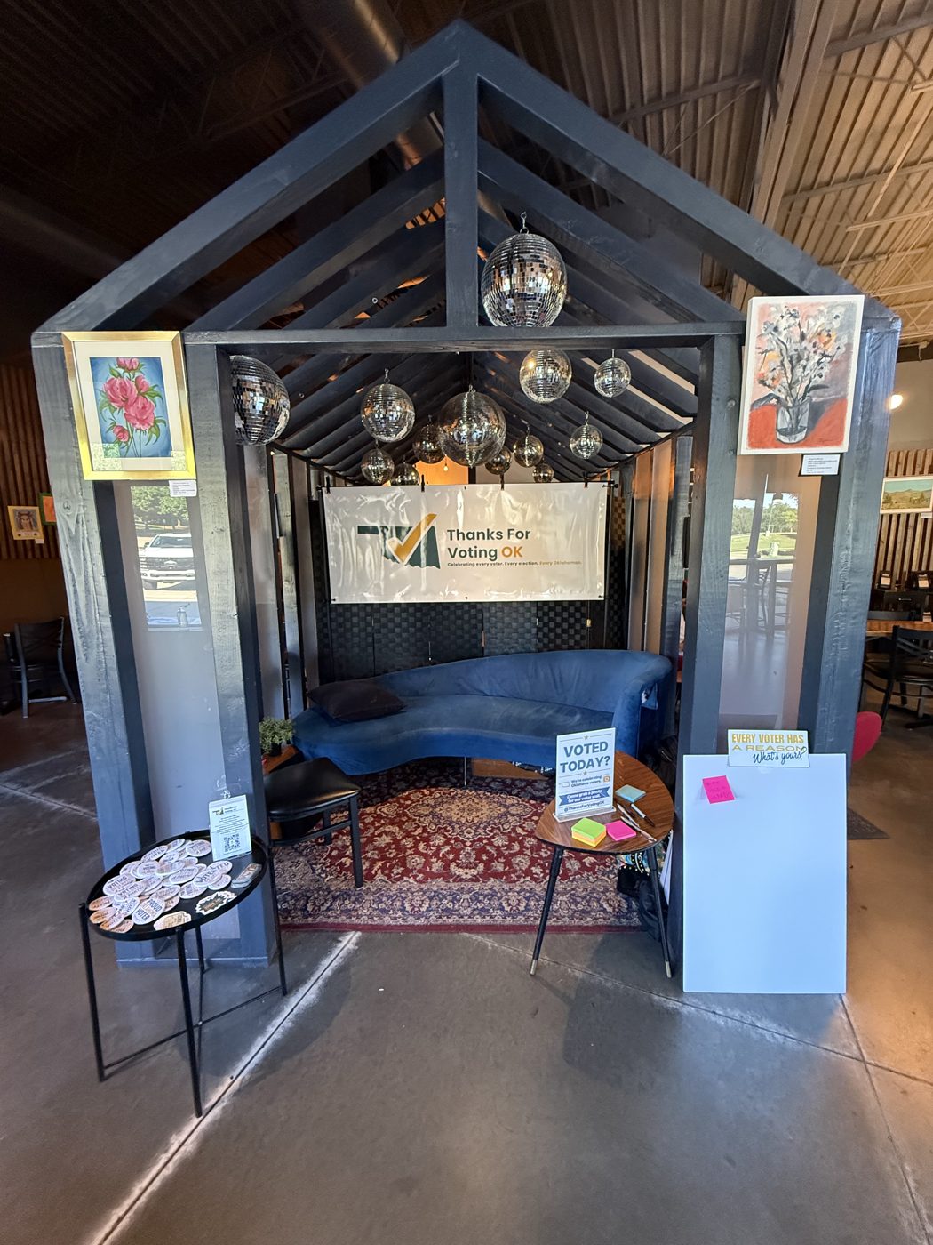 The Thanks For Voting OK photo booth: a wooden pergola hung with disco balls and a TFVOK banner, a blue couch, and a table of I Voted stickers